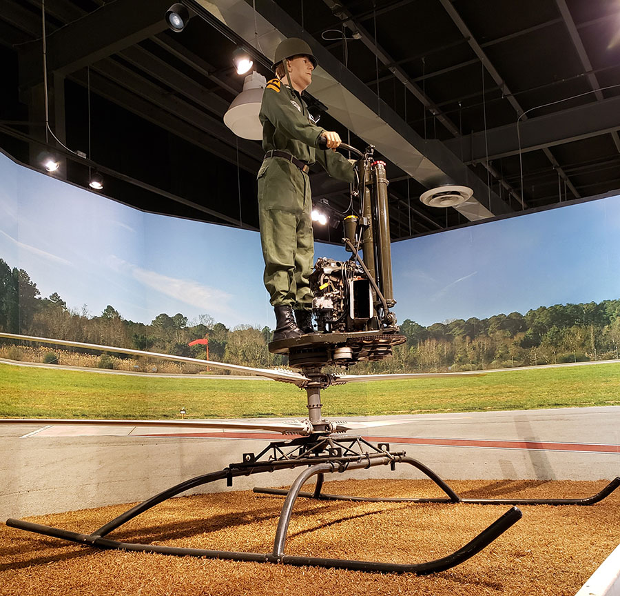 A museum exhibit inside the US Army Transportation Museum including a Soldier standing on a contraption.